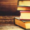 Stack of hardcover books on wooden surface.