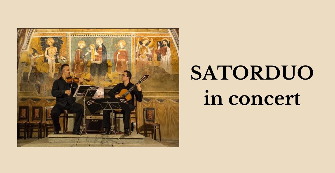 SATORDUO in concert. Photo of a man playing violin and a man playing guitar. They are seated in front of sacred frescoes.